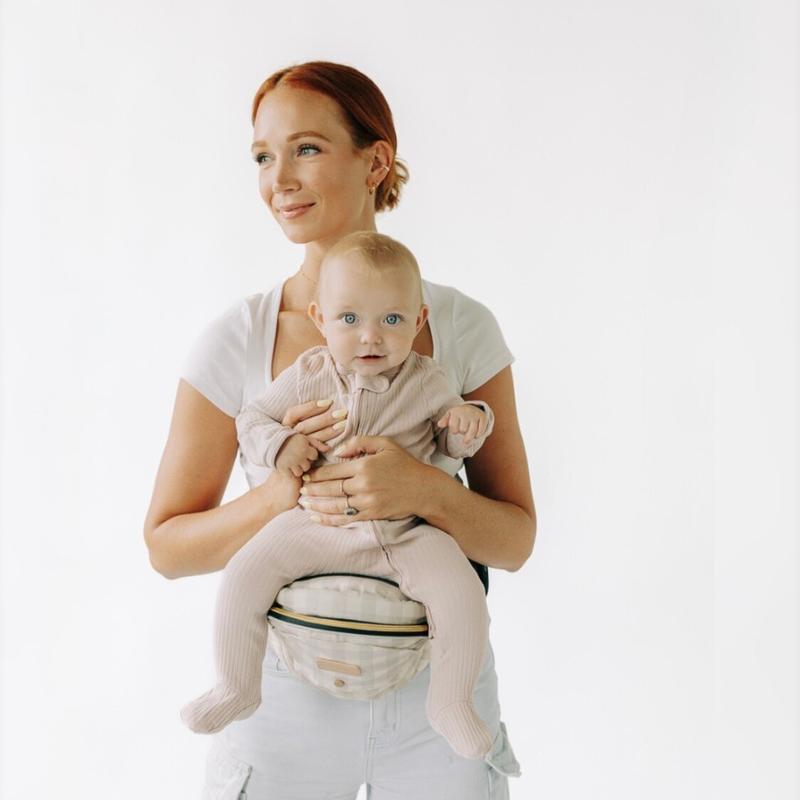 Woman holding a baby in a hip seat carrier against a white background