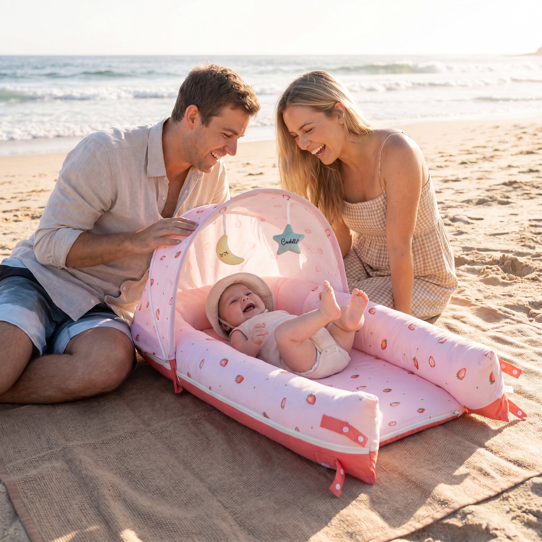 Family with baby in portable JollyBoo deluxe infant lounger with sunshade at the beach, Blush Strawberry print