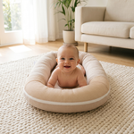 Awake baby doing supervised tummy time in beige newborn lounger on a knit rug