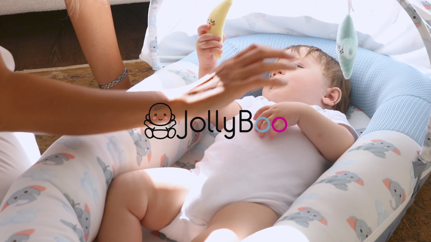 Baby playing with toys in JollyBoo blue elephant infant lounger, supervised tummy time and lounging in baby nest, pink strawberry, green leaves, beige loungers